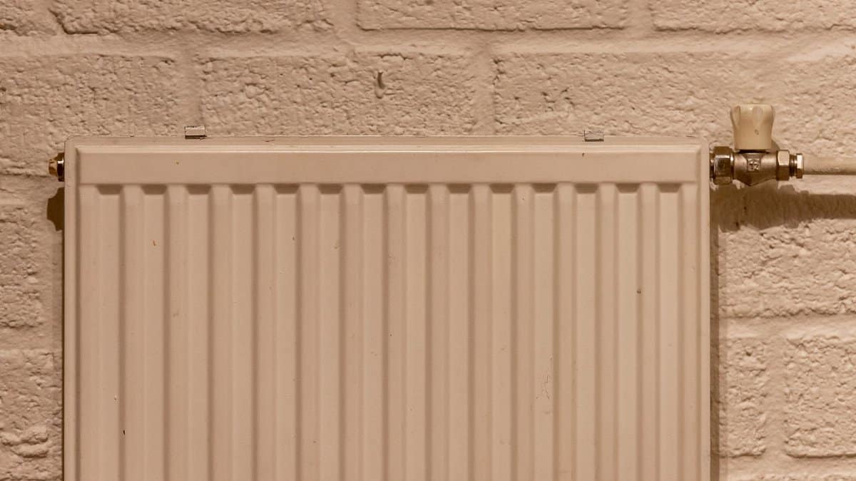 A clean white radiator mounted on a textured brick wall, indoors and well-lit.