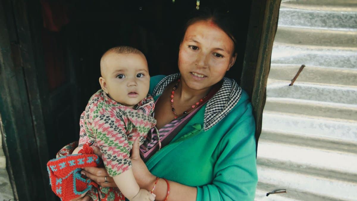 A mother holding her baby in a rural doorway, showing warmth and care.