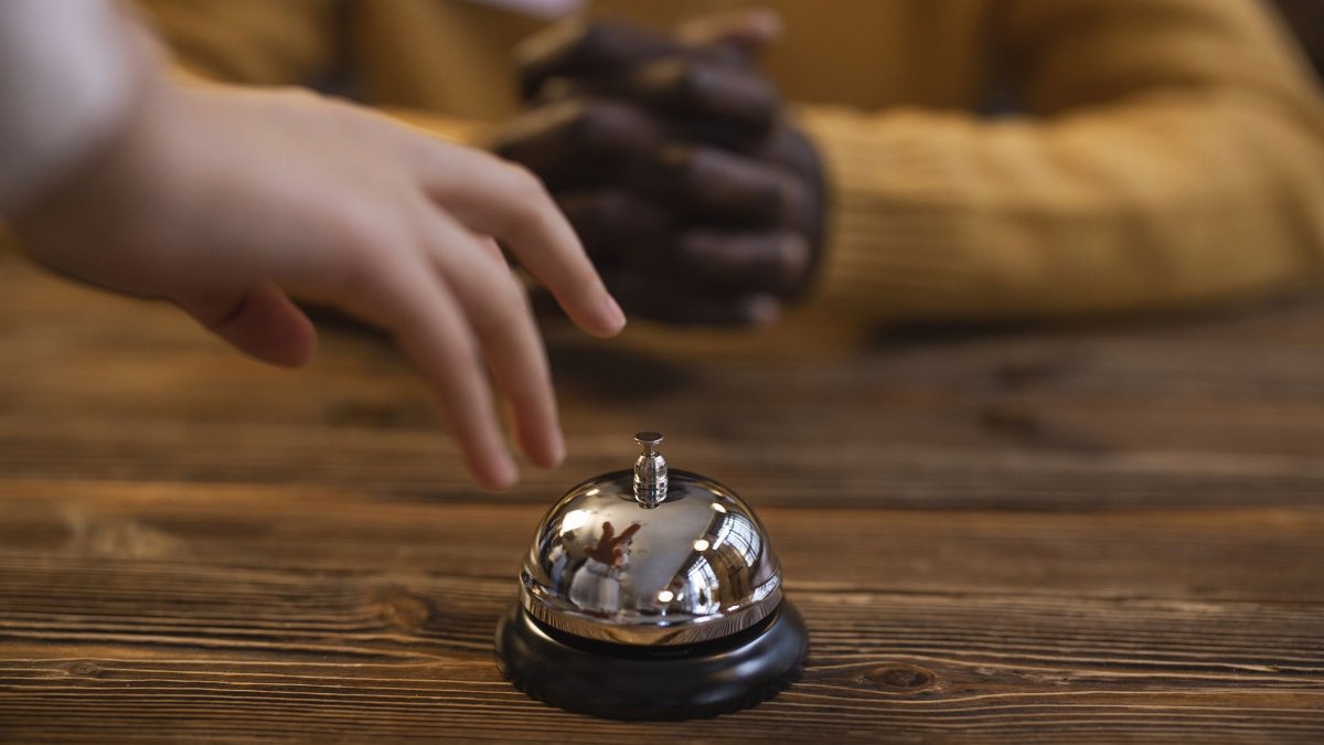 A hand reaching for a reception bell on a wooden table, indicating service or hospitality request.