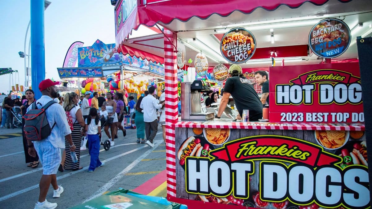 Bustling outdoor fair with a popular hot dog stand and diverse crowd.