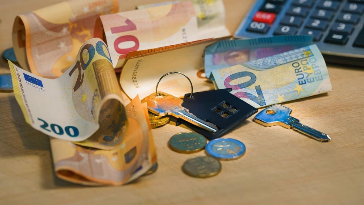 Euro banknotes and coins with house keys on a table symbolize finance and real estate.