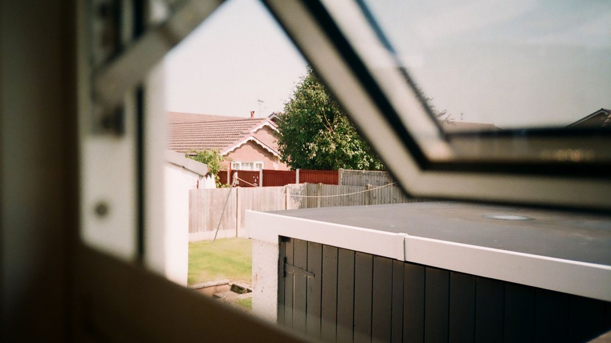 A serene view of a suburban backyard seen through an open window, capturing houses and greenery.