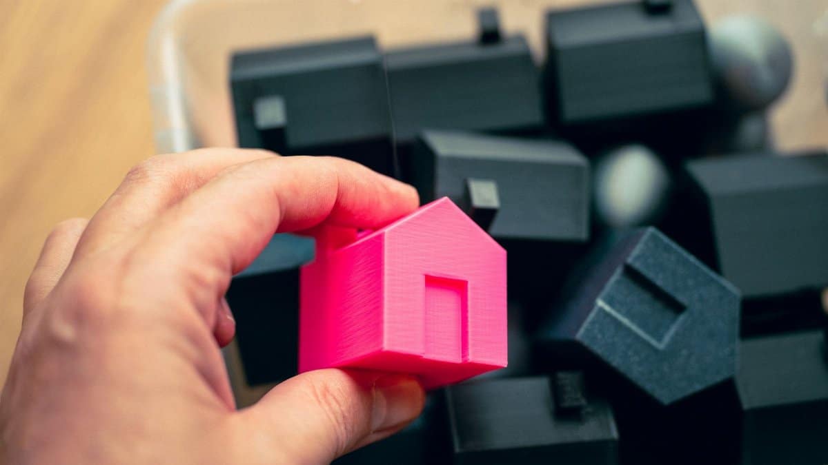Hand selecting a pink house model from a box of miniature homes, symbolizing real estate choices.
