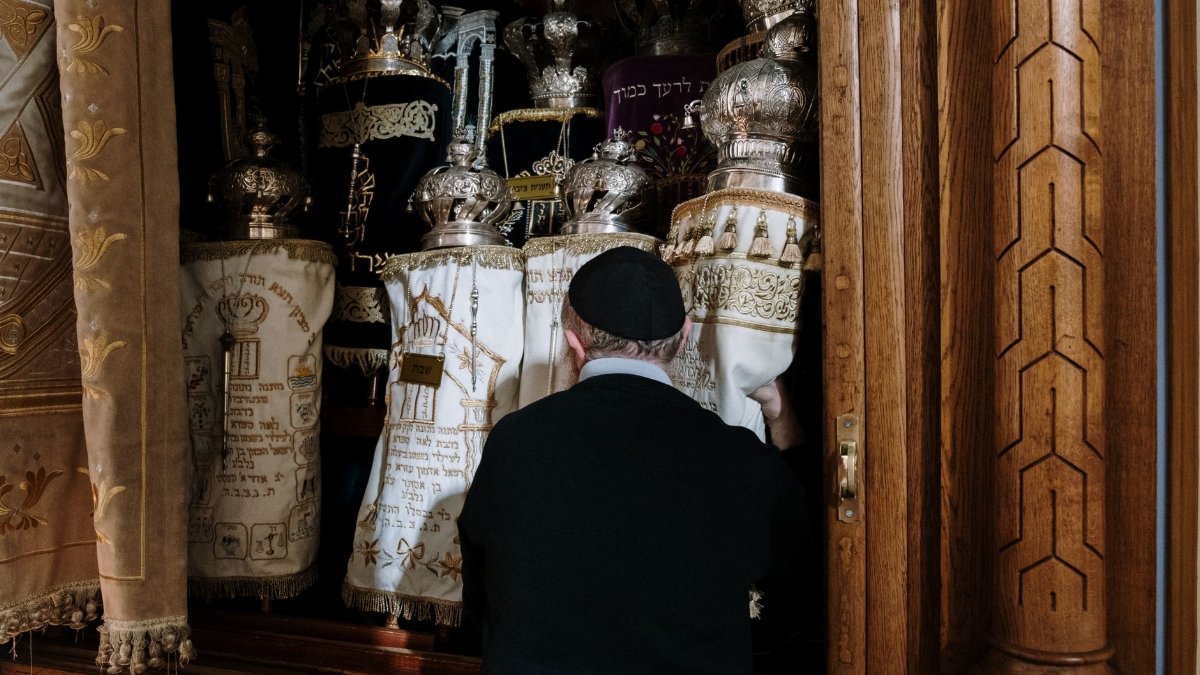 Rabbi standing before Torah ark, holding scrolls, in a synagogue, symbolizing Jewish tradition.