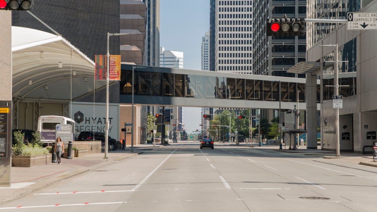 Sunlit street scene in downtown Houston featuring city skyline and modern pedestrian bridge.