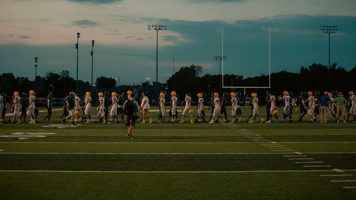 Players walking off football field at dusk after the game ends.