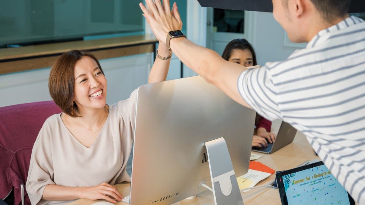 Group of professionals celebrating with a high five at their office desk, promoting teamwork and cooperation.