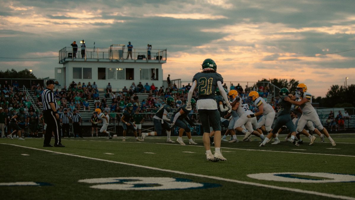 High school football game at sunset with players and crowd in action.