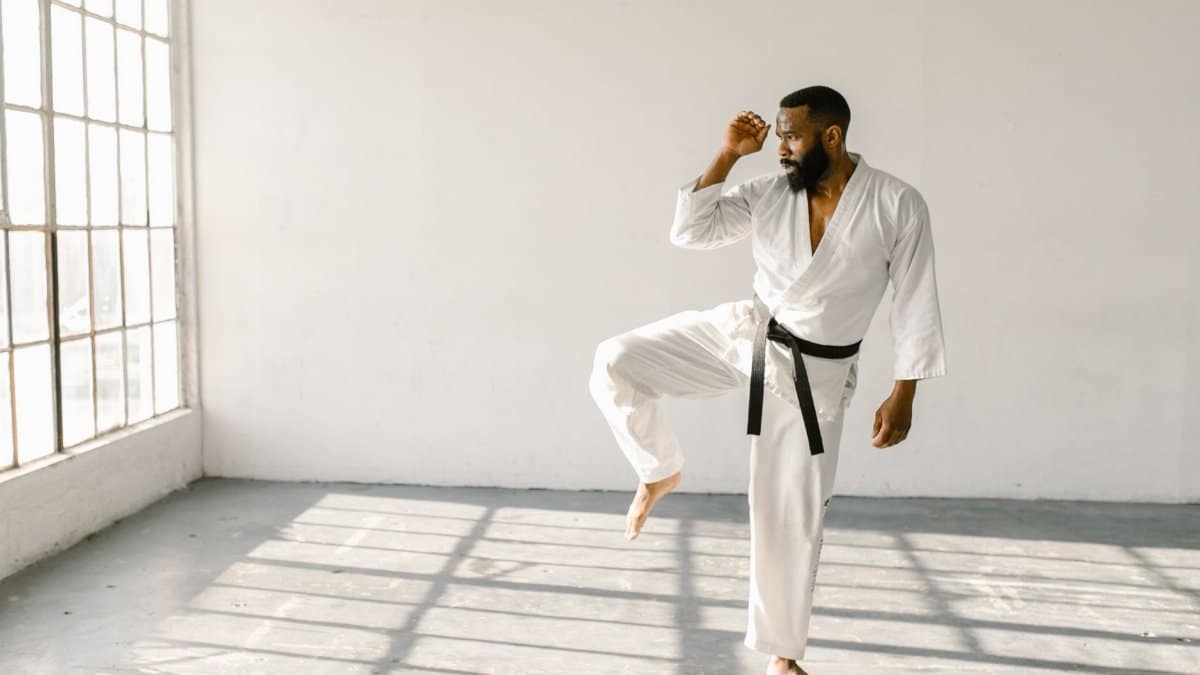 African American man practicing karate in a sunlit empty room with glass windows.