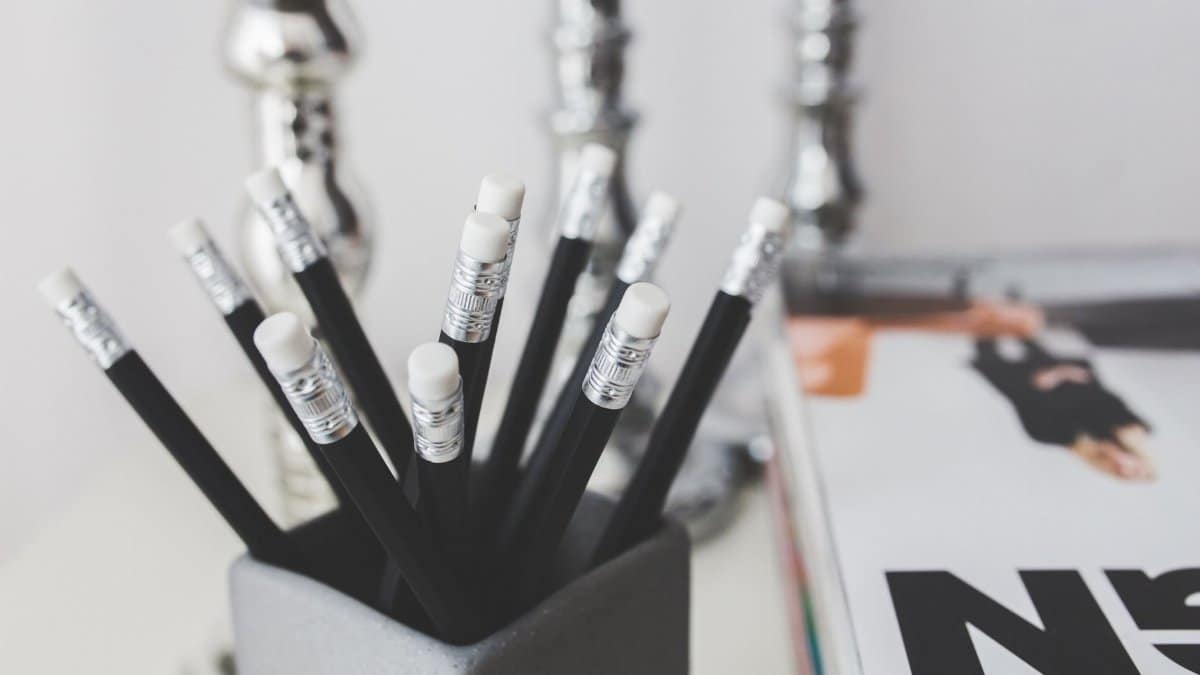 Black pencils with erasers in a holder on a minimalistic desk setup.