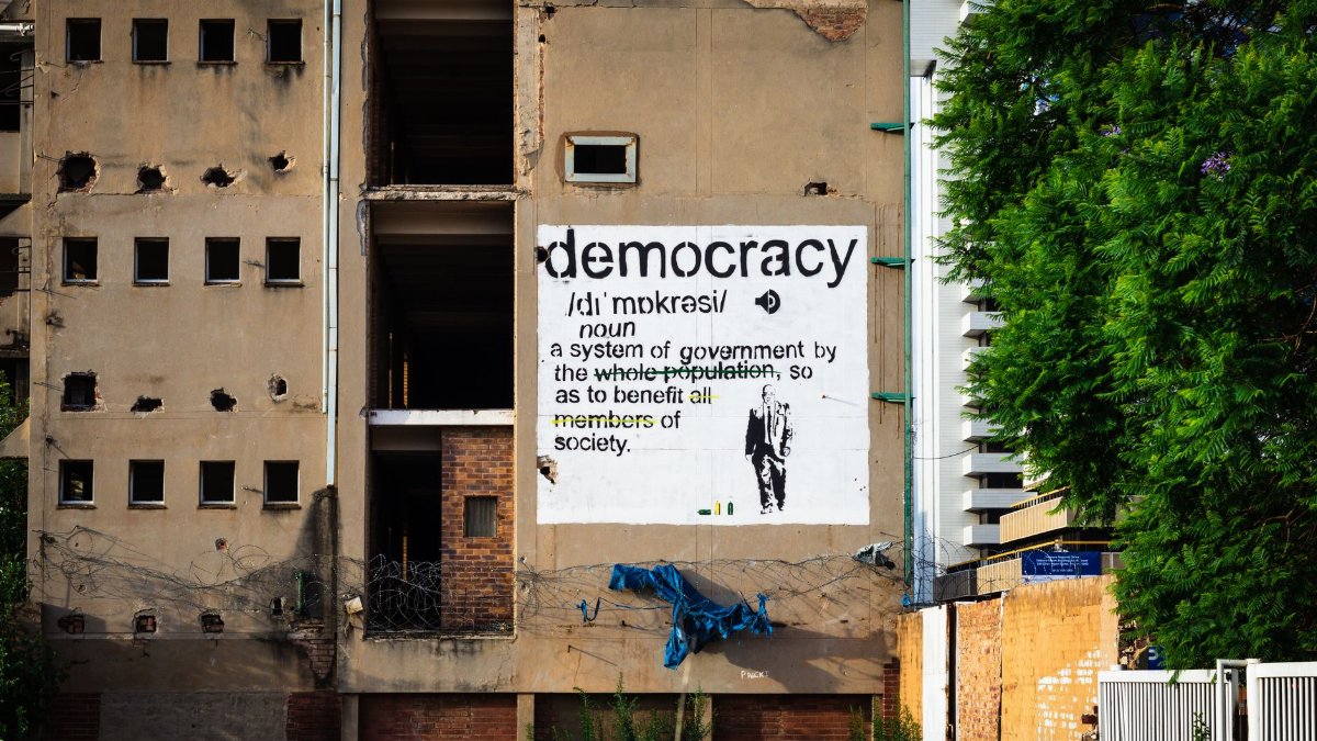 An abandoned building features a prominent democracy poster amidst urban decay.