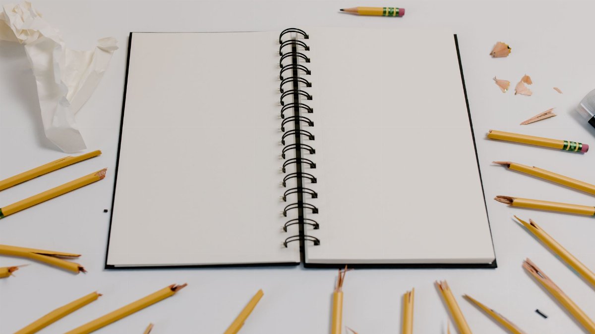 A spiral notebook surrounded by broken pencils and crumpled paper on a white background, ready for creative brainstorming.