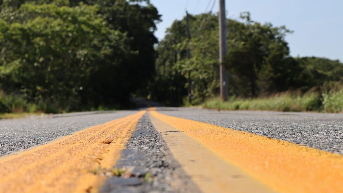 Close-up view of a country road with vibrant yellow center lines and lush green surroundings.