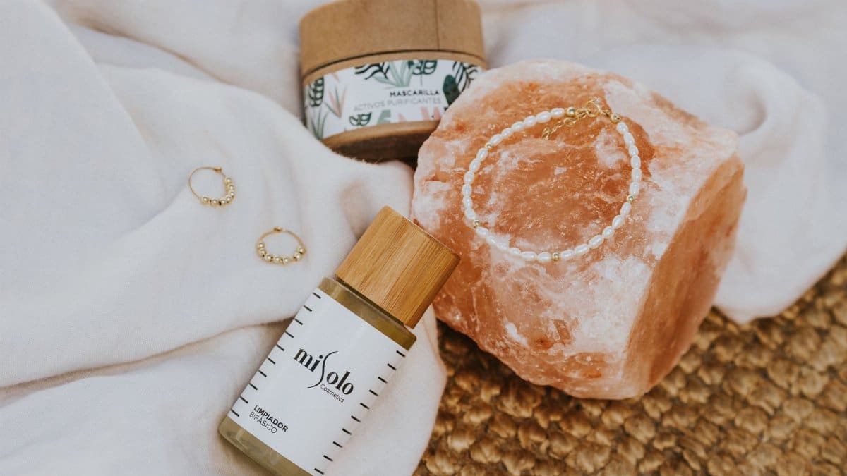 A flat lay of natural skincare products, a mineral stone, and jewelry on fabric.