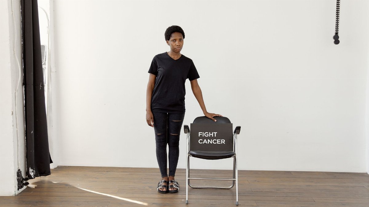 Woman standing next to a chair with 'Fight Cancer' text, promoting cancer awareness.
