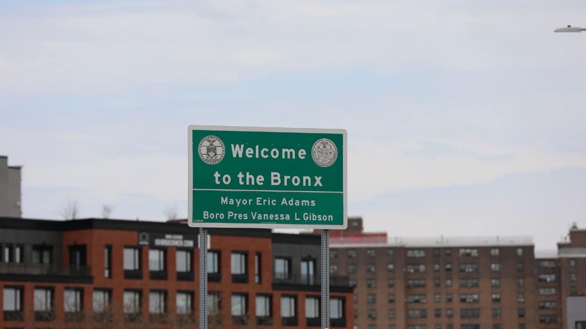 A cityscape featuring the Welcome to the Bronx sign in New York City, with residential buildings in the background.
