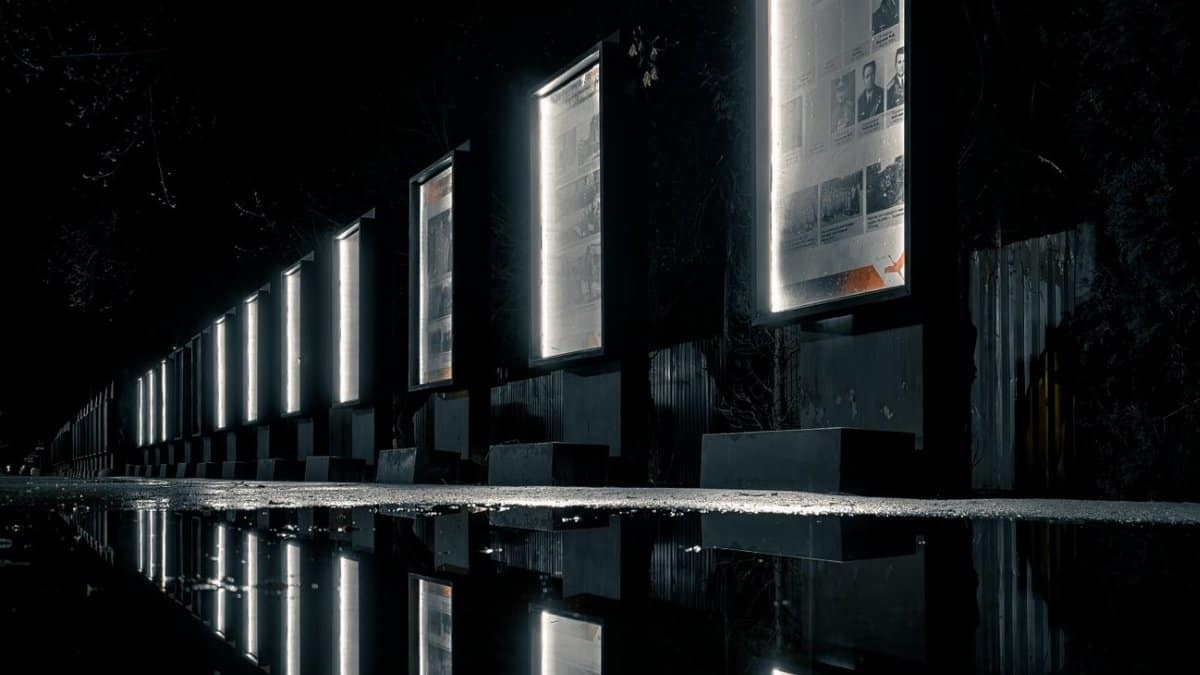 Illuminated billboards at night reflecting on a wet surface outdoors creating a mysterious scene.