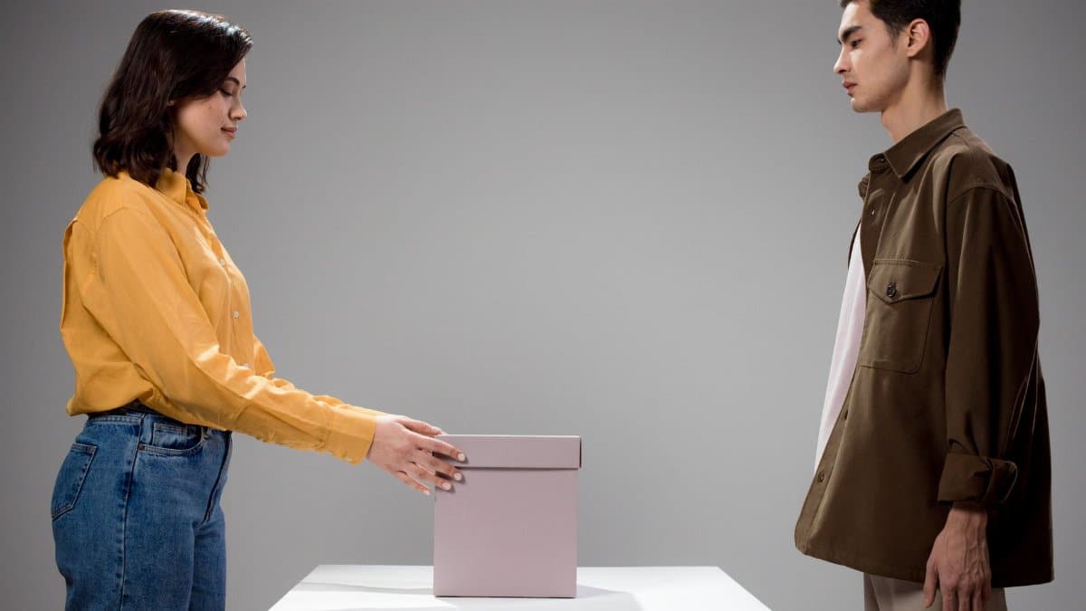 A man and woman standing opposite each other in a studio with a gift box in between.