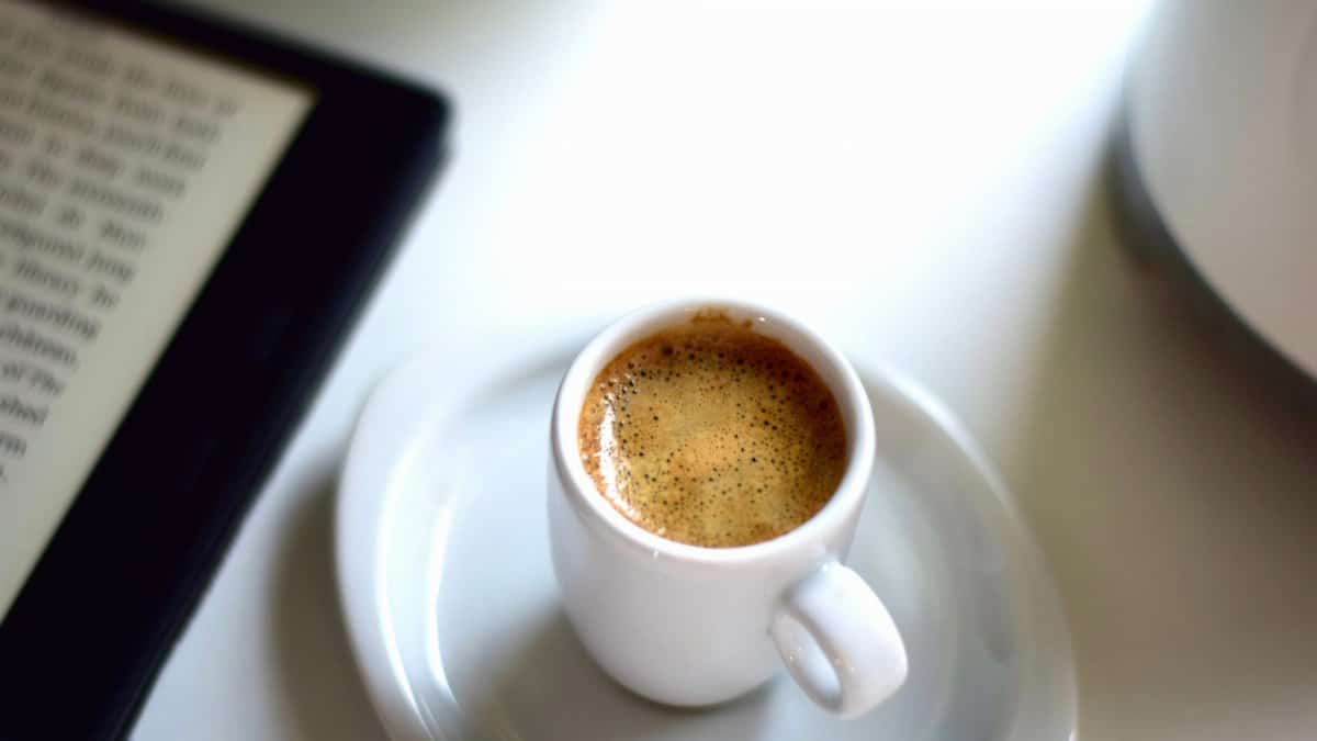 A steaming espresso with an e-reader on a bright morning setup.