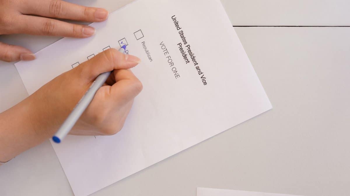Hand placing vote on ballot form during election process, highlighting civic duty and democracy.