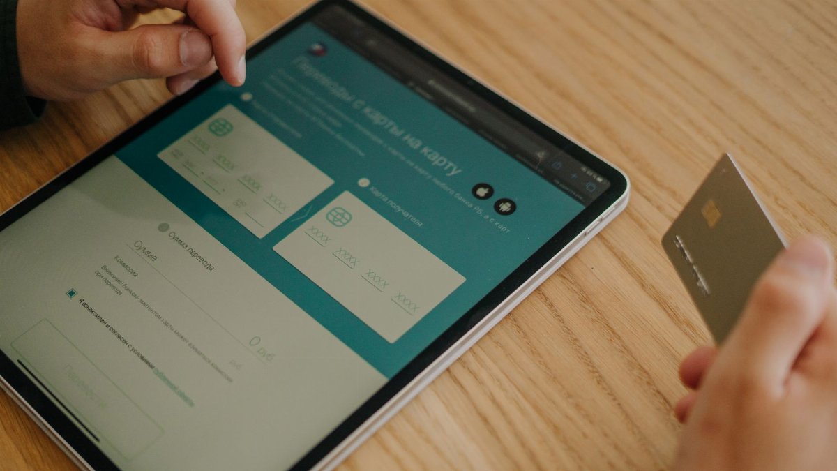 Hands making an online purchase using a tablet and credit card on a wooden table.