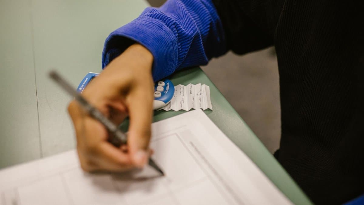Close-up shot of a student writing on a test paper, hinting at cheating with a note.