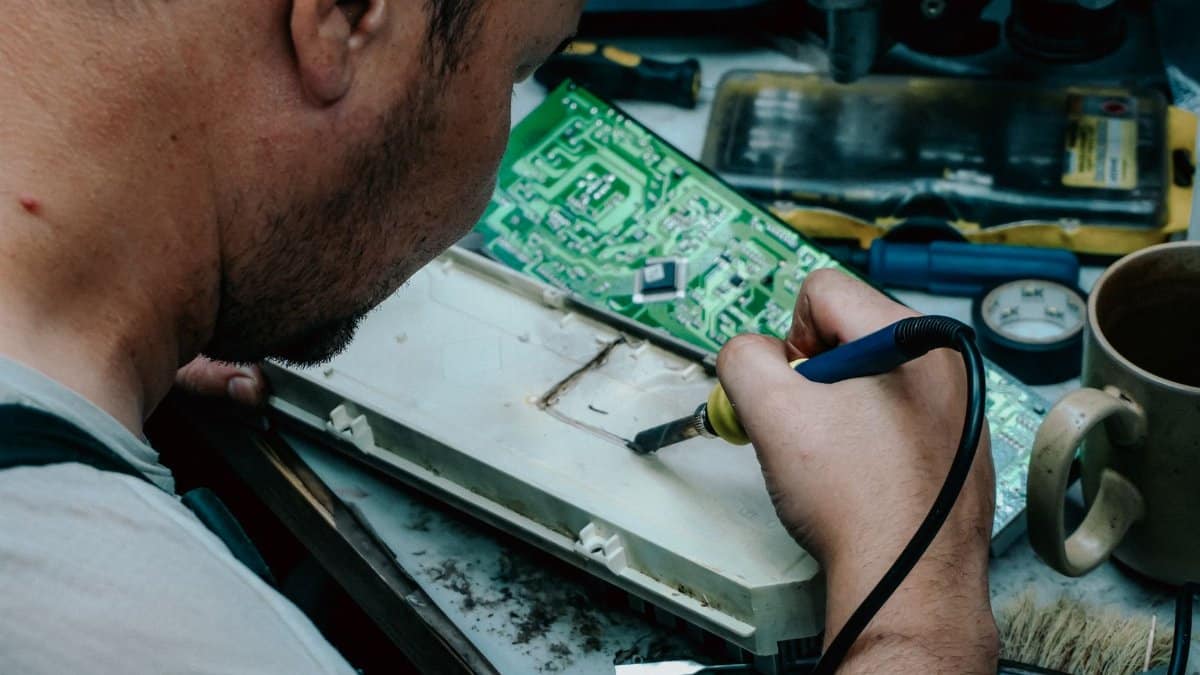 A focused technician using a soldering iron to repair electronic components at a workstation.