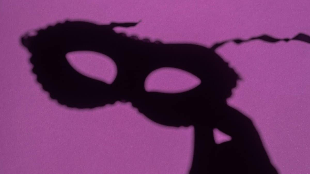 Shadow of a lace mask creates an intriguing silhouette on a vibrant purple backdrop. Ideal for mysterious themes.
