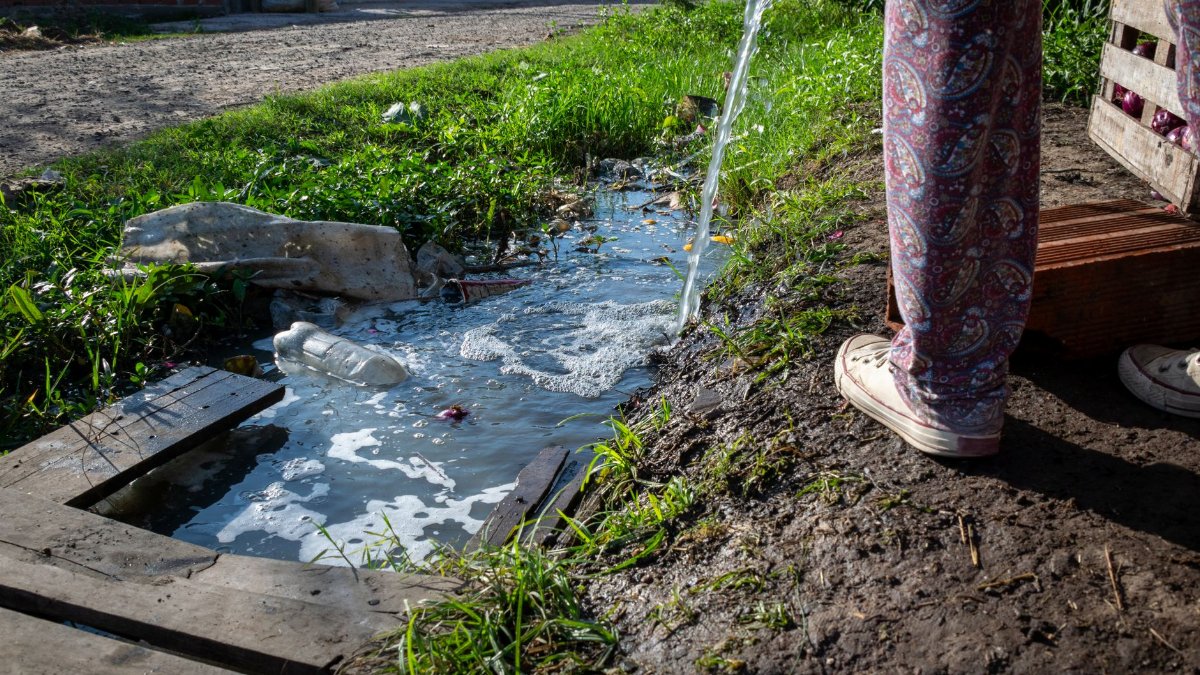 A polluted stream with waste in an Argentine neighborhood. Highlights water pollution issues.