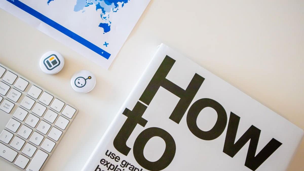 Stylish desk setup with a how-to book, keyboard, and world map on paper.