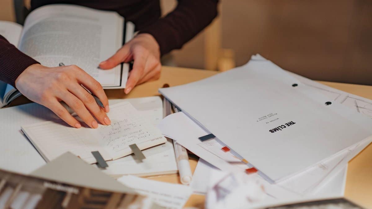 Close-up of a woman's hands writing notes in a notebook for a research project indoors.