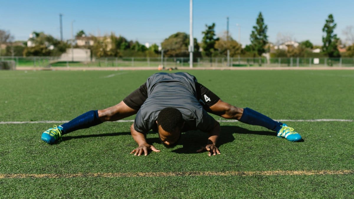 Athlete performing a stretching exercise on a sunny soccer field, focusing on fitness and flexibility.
