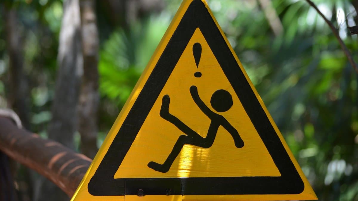 Yellow triangular warning sign indicating slippery surface in lush forest setting.