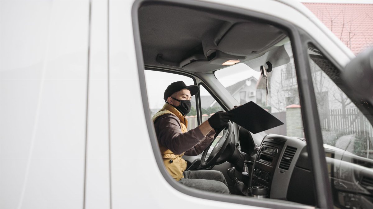 Masked delivery person inside a van holding a clipboard, illustrating modern delivery service.