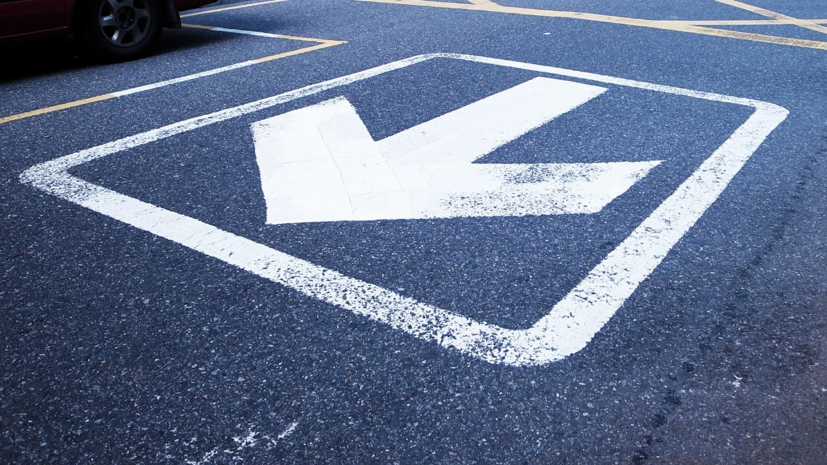 Close-up shot of a white arrow painted on asphalt indicating direction.