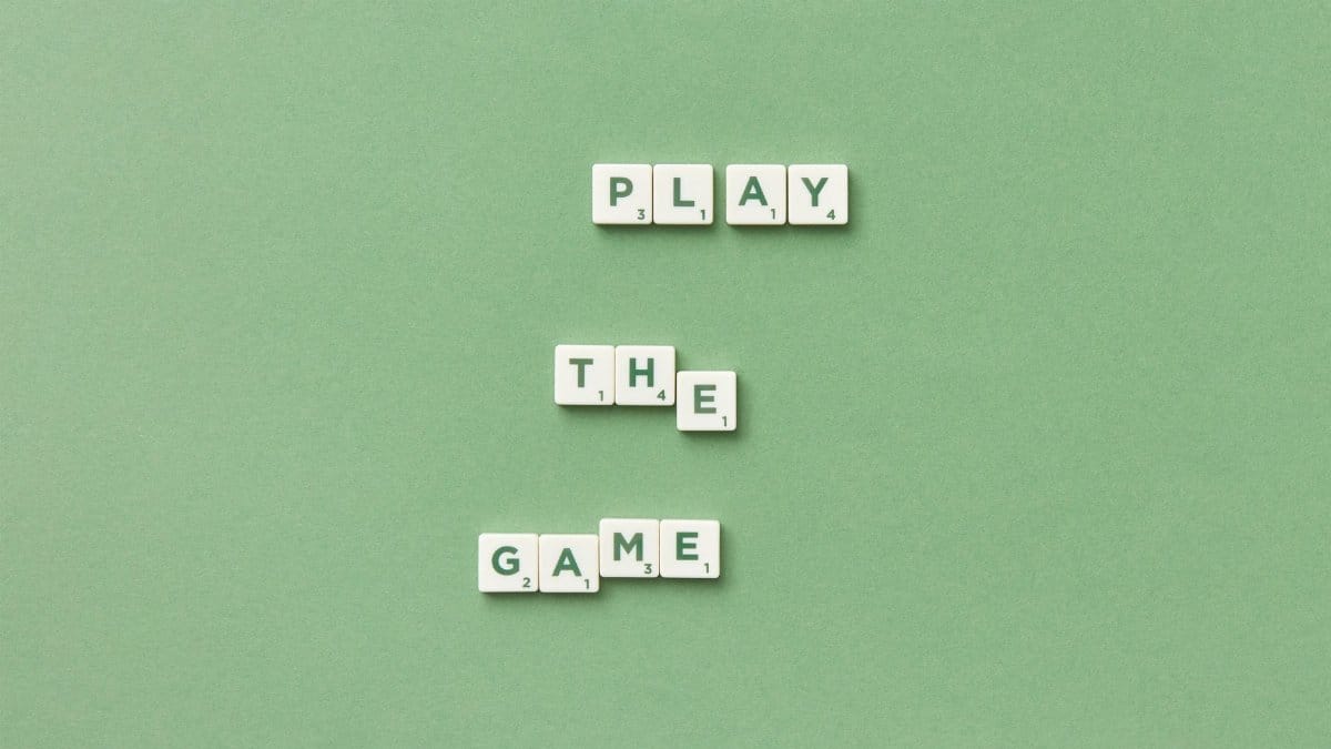 Scrabble letter tiles spelling 'Play the Game' on light green background.