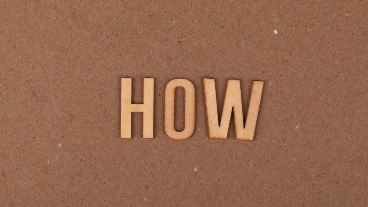 Wooden letters spelling 'HOW' on brown textured cardboard background.