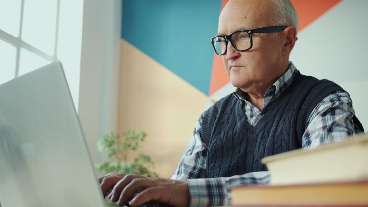Elderly man focused on typing at his laptop in a bright, stylish office.