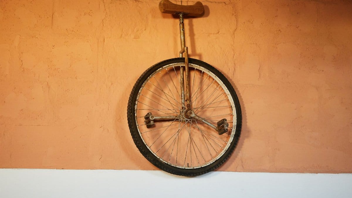 Retro one wheel bicycle with rusty rack and brown seat hanging on brick orange wall