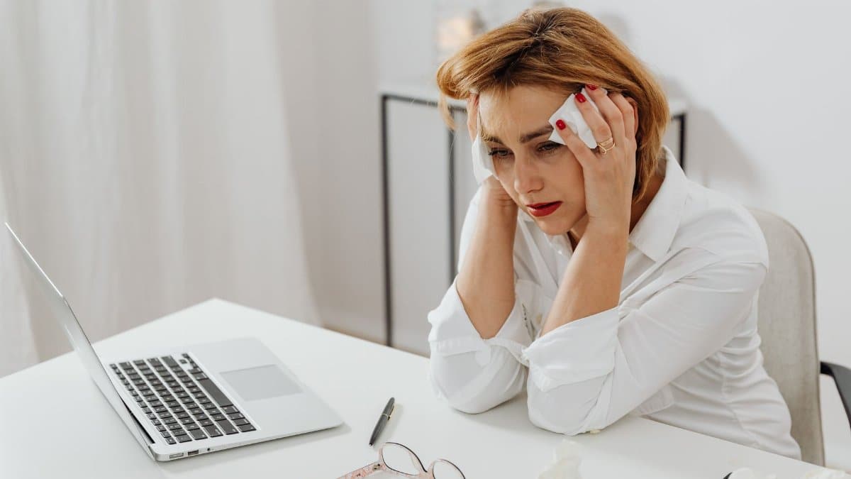 A woman in distress at her office desk, surrounded by tissues and a laptop.