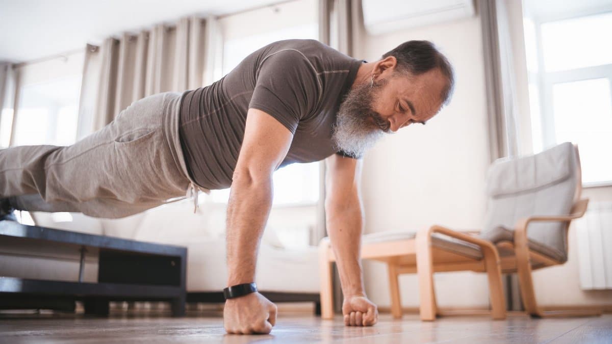 Elderly man performing push-ups at home in a bright and airy living room.