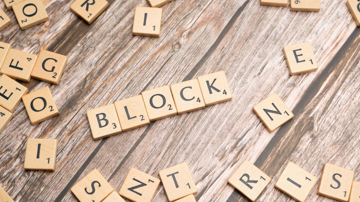 Scrabble tiles arranged to spell 'Block' on a textured wooden background.
