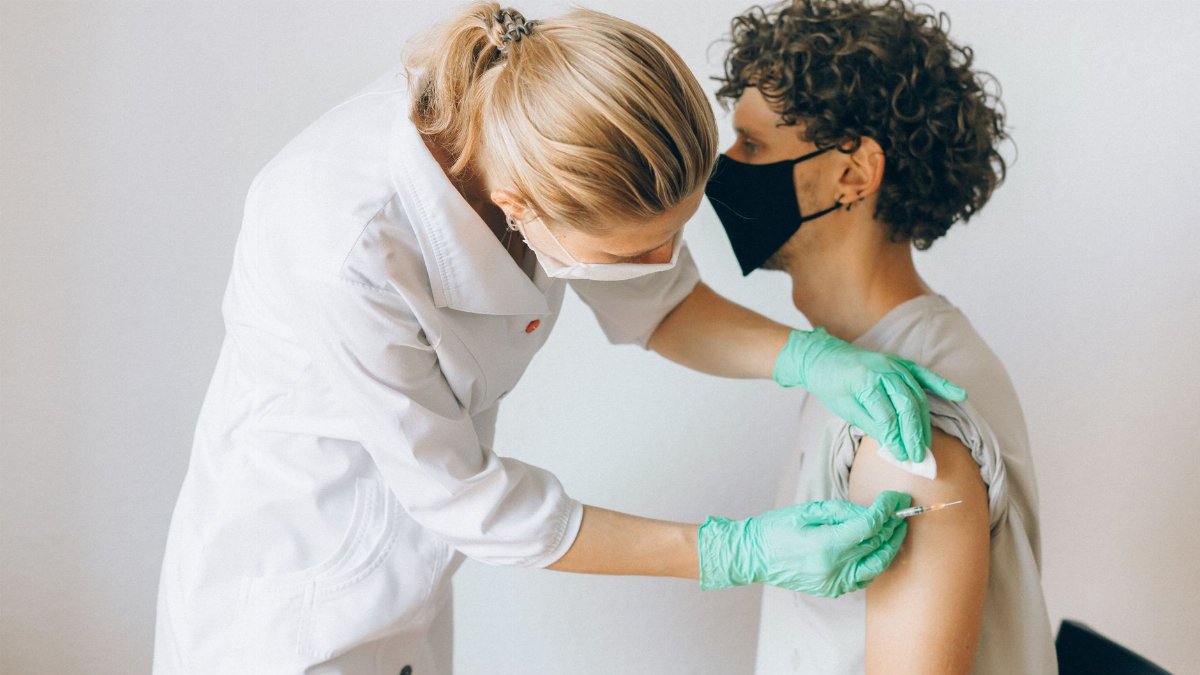 A healthcare worker gives a vaccine shot to a patient wearing a mask, highlighting medical safety and health precautions.