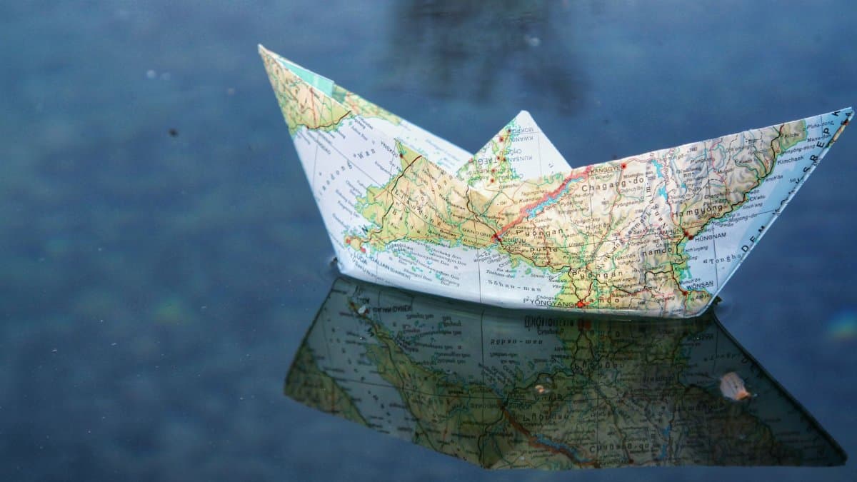 A paper boat folded from a map floats on water, creating a unique reflection.