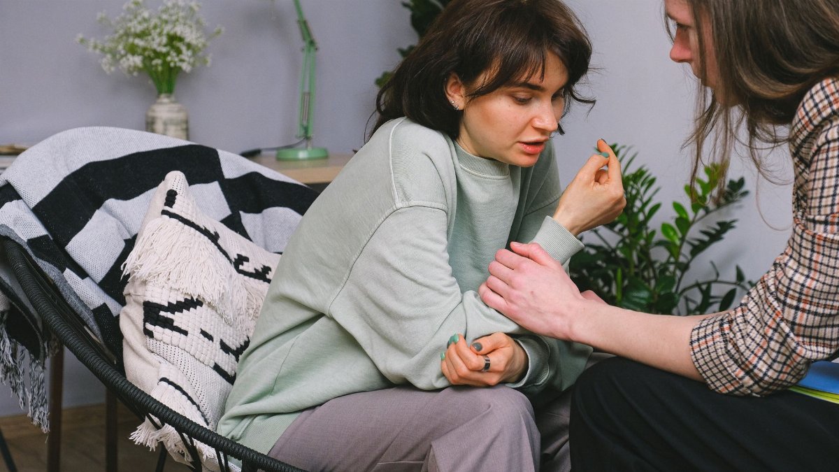 Crop psychotherapist holding adult woman by arm while talking during psychological session in light house