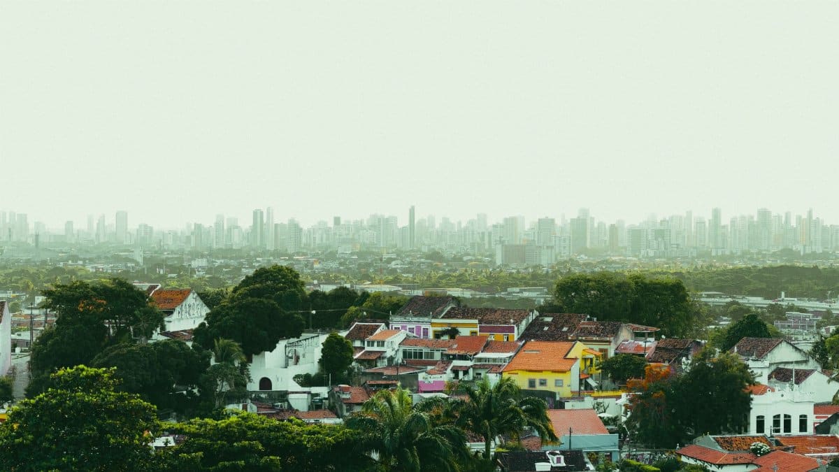 A vibrant, panoramic view of Olinda's colorful colonial architecture with Recife skyline in the distance.
