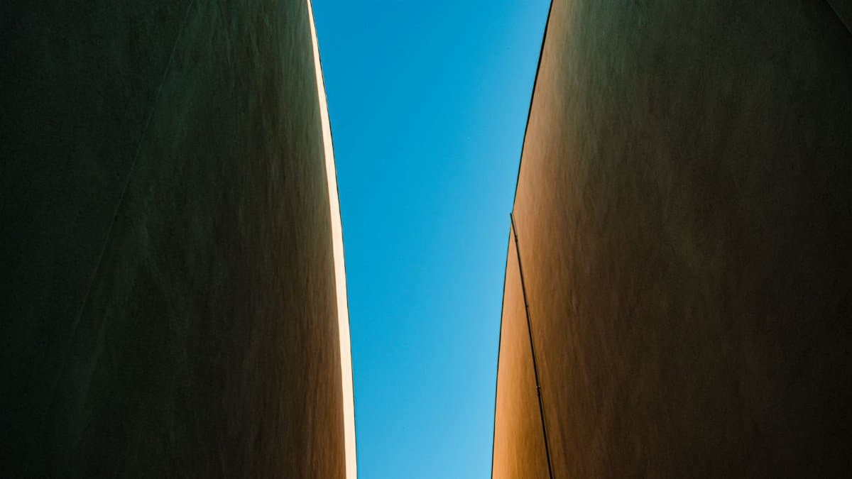 A minimalist perspective of a narrow gap between modern buildings under a bright blue sky.