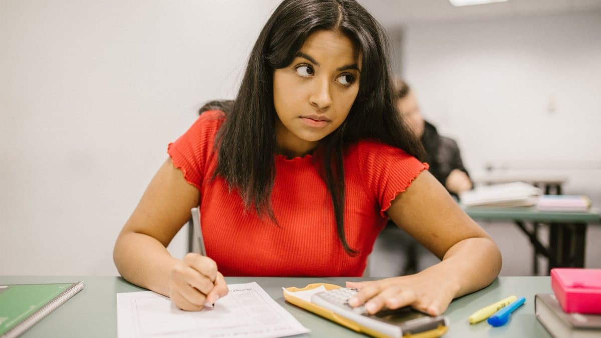 Focused student in a red shirt using a calculator during a classroom exam.