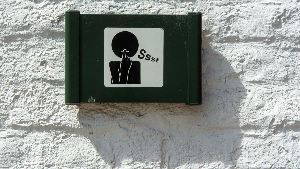 A green sign on a white brick wall indicating silence with a 'Ssst' symbol.