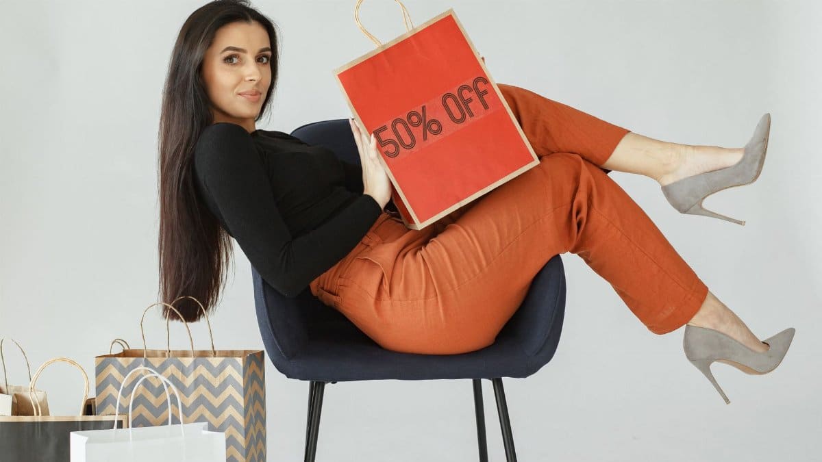 Stylish woman in chic pose holding a 50% off shopping bag, surrounded by bags.